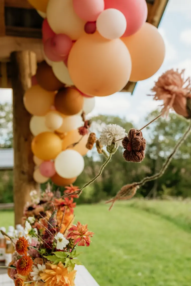 Detal girlandy w beżach i pomarańczach z suszonymi kwiatami wplecionymi między balony