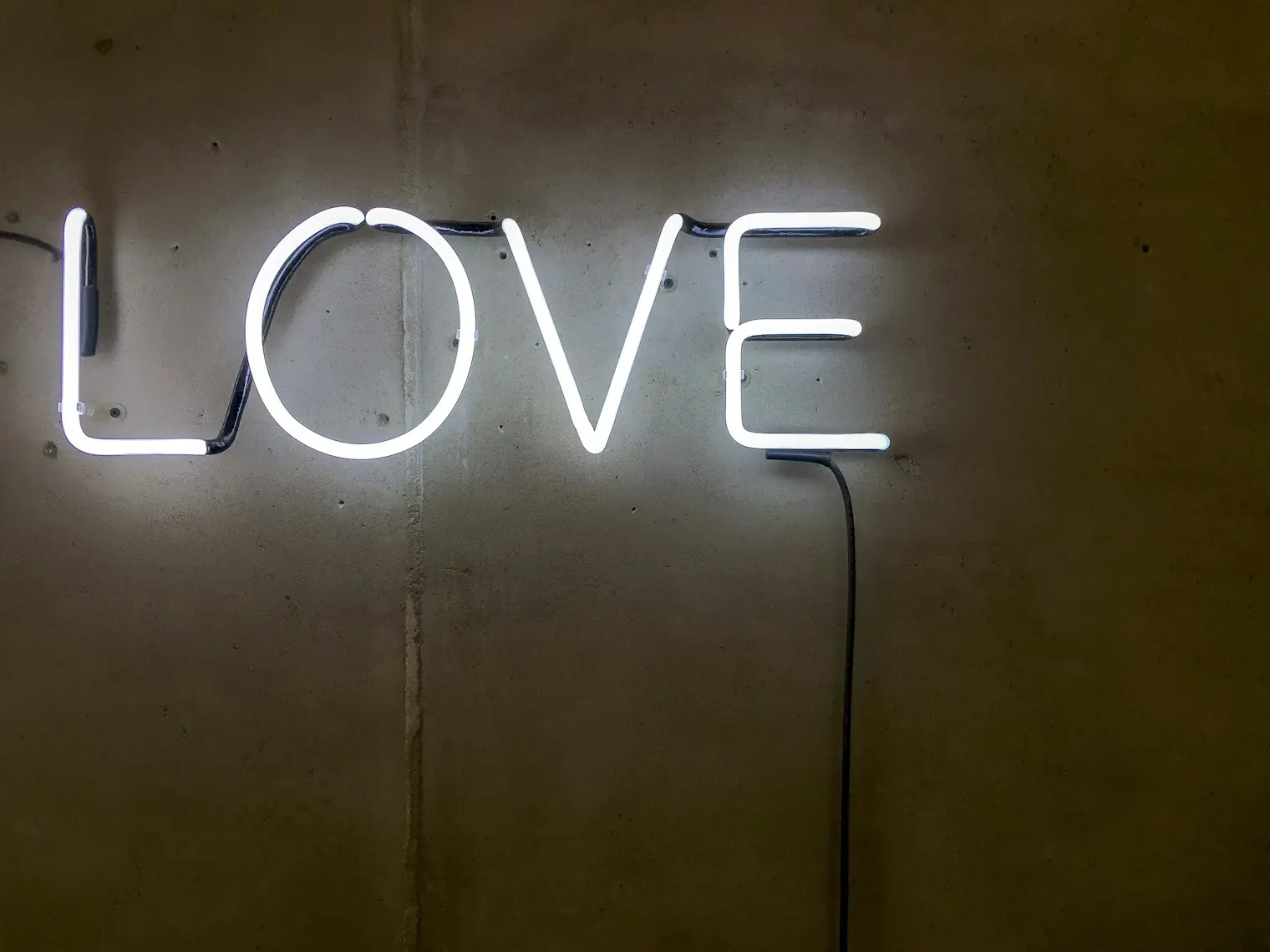 Biały neon z napisem LOVE zawieszony na ciemnej ścianie sali
